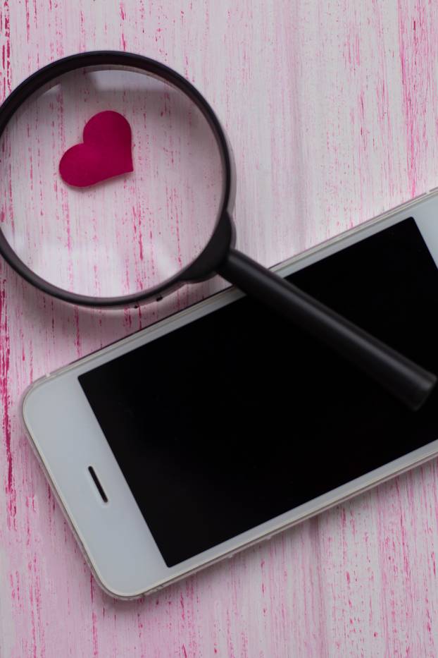heart under a magnifying glass, lies near a white mobile phone. 
