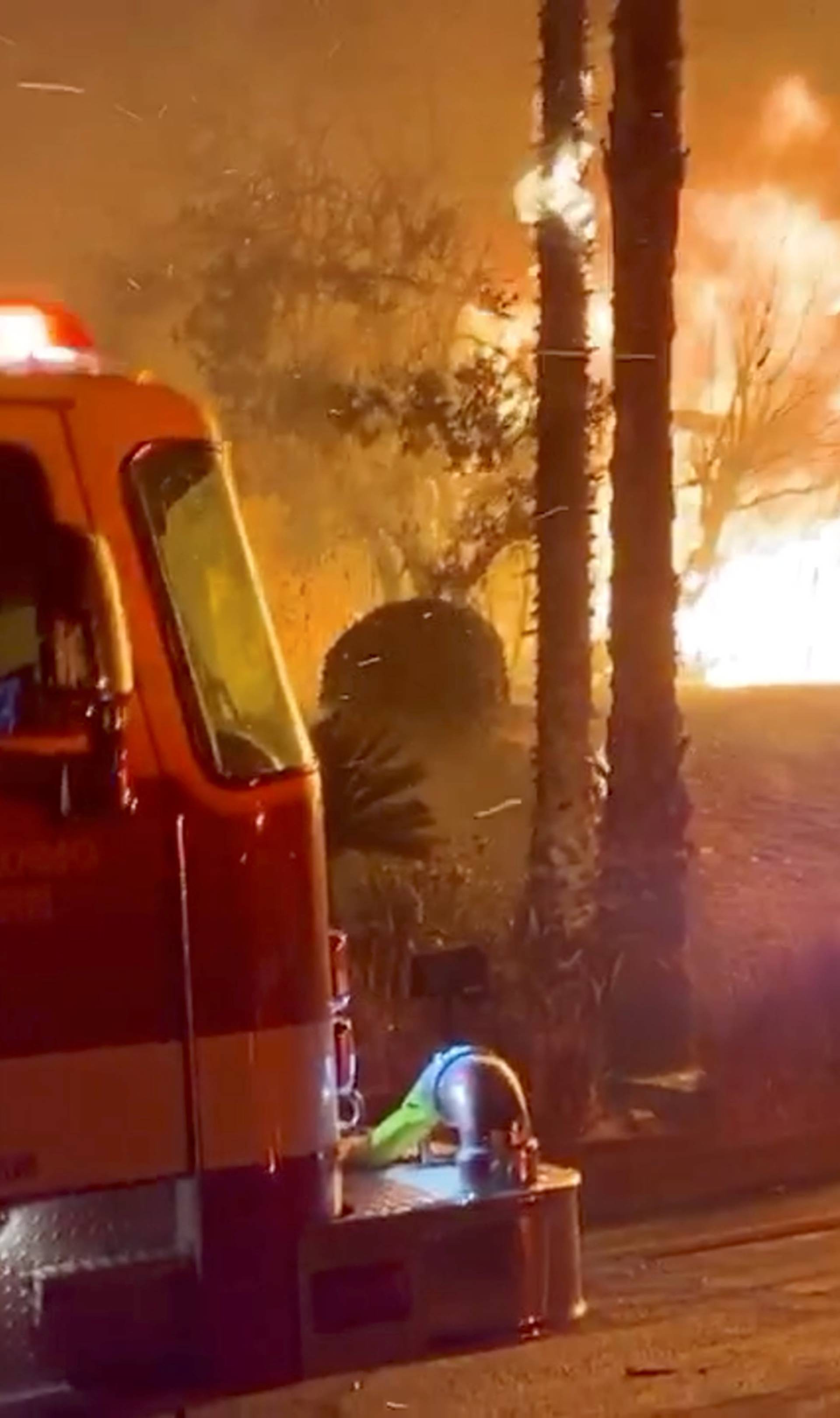 A firefighter passes by a fire engine in front of a burning house during wildfires in San Bernardino, California