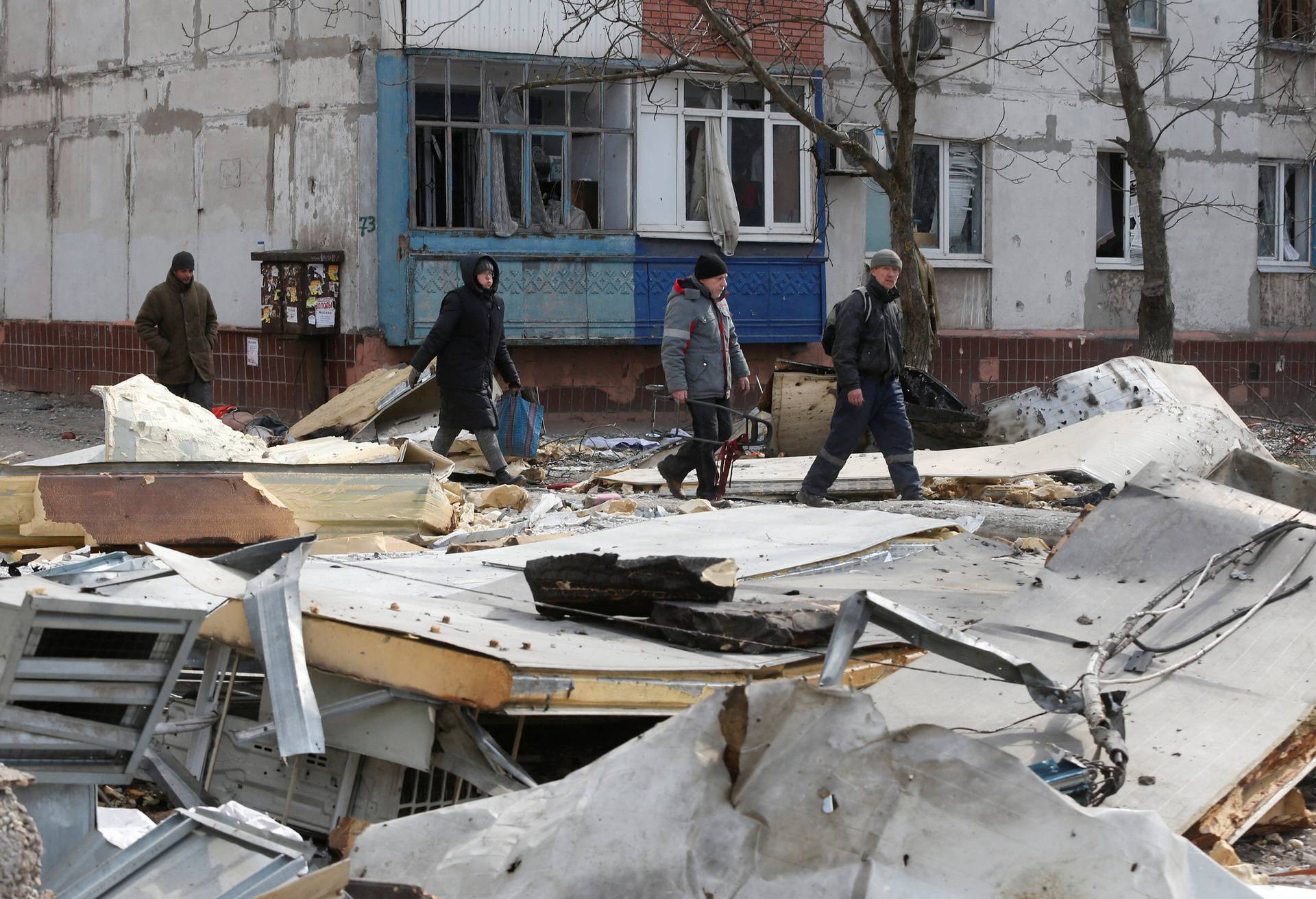 Local residents walk past a damaged residential building in the besieged city of Mariupol