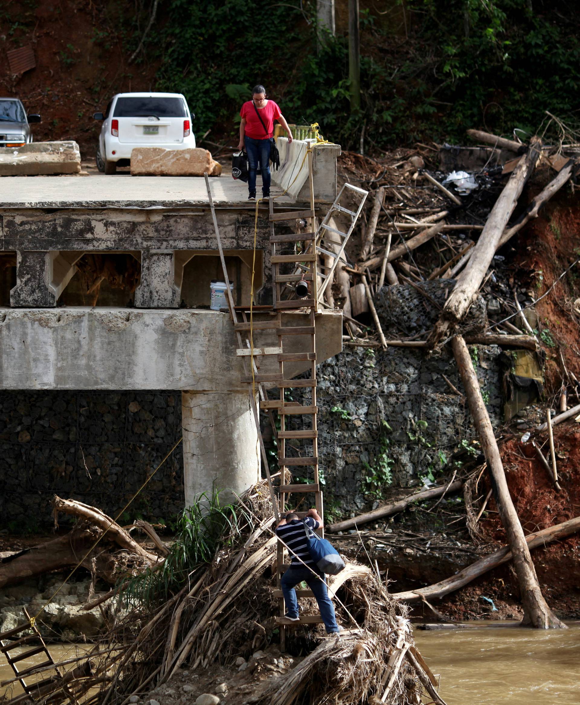 FILE PHOTO: A woman looks as her husband climbs down a ladder at a partially destroyed bridge, after Hurricane Maria hit the area in September, in Utuado