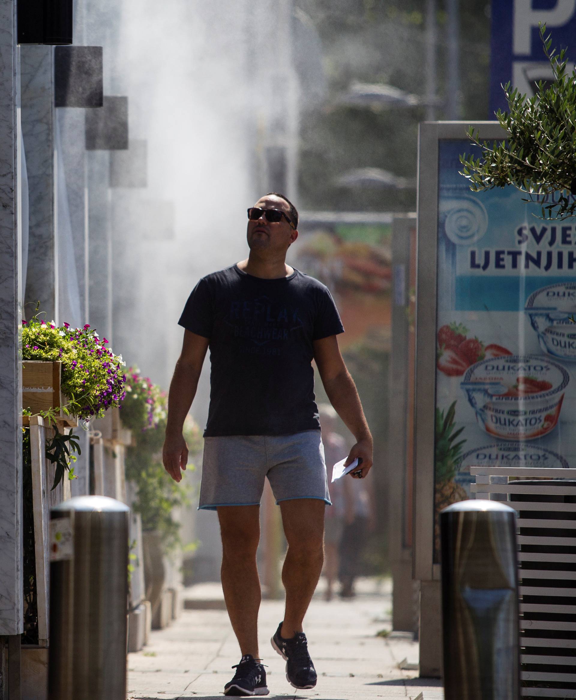 A man cools off under the mist of water sprinklers on a hot summer day in Podgorica