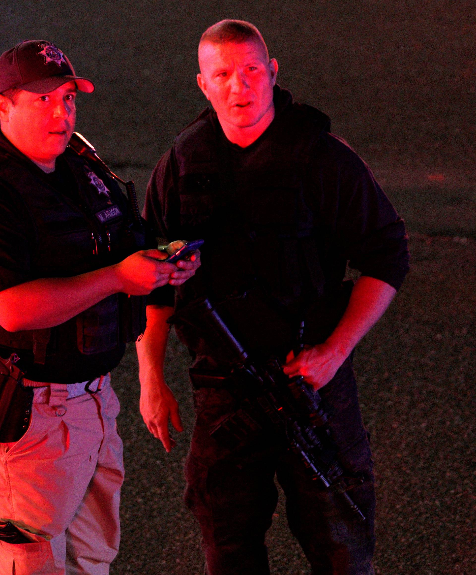 Police compare an image on a smartphone to a person they spotted in the crowd at the scene of a shooting at a Walmart in Thornton