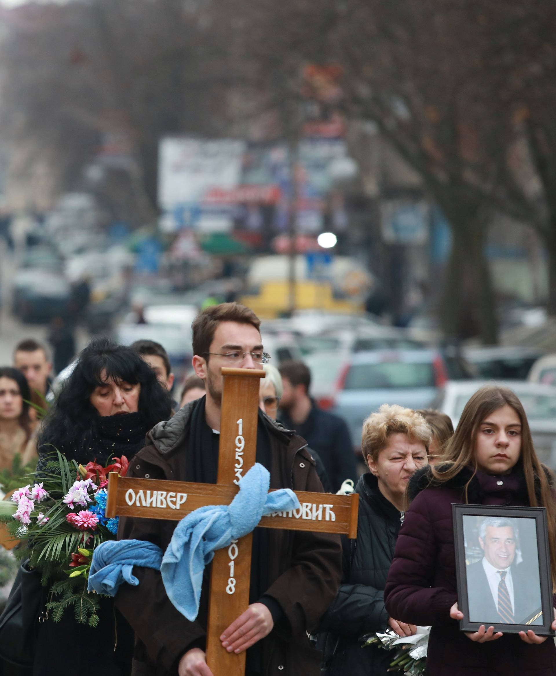 A cortege escorts a car carrying coffin of Oliver Ivanovic, flanked by priests and family,  to the northern outskirts of Kosovska Mitrovica
