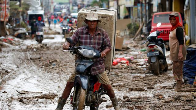 Man carrying a washing machine rides a motorbike as he collects items at a residential area affected by floods in Bekasi