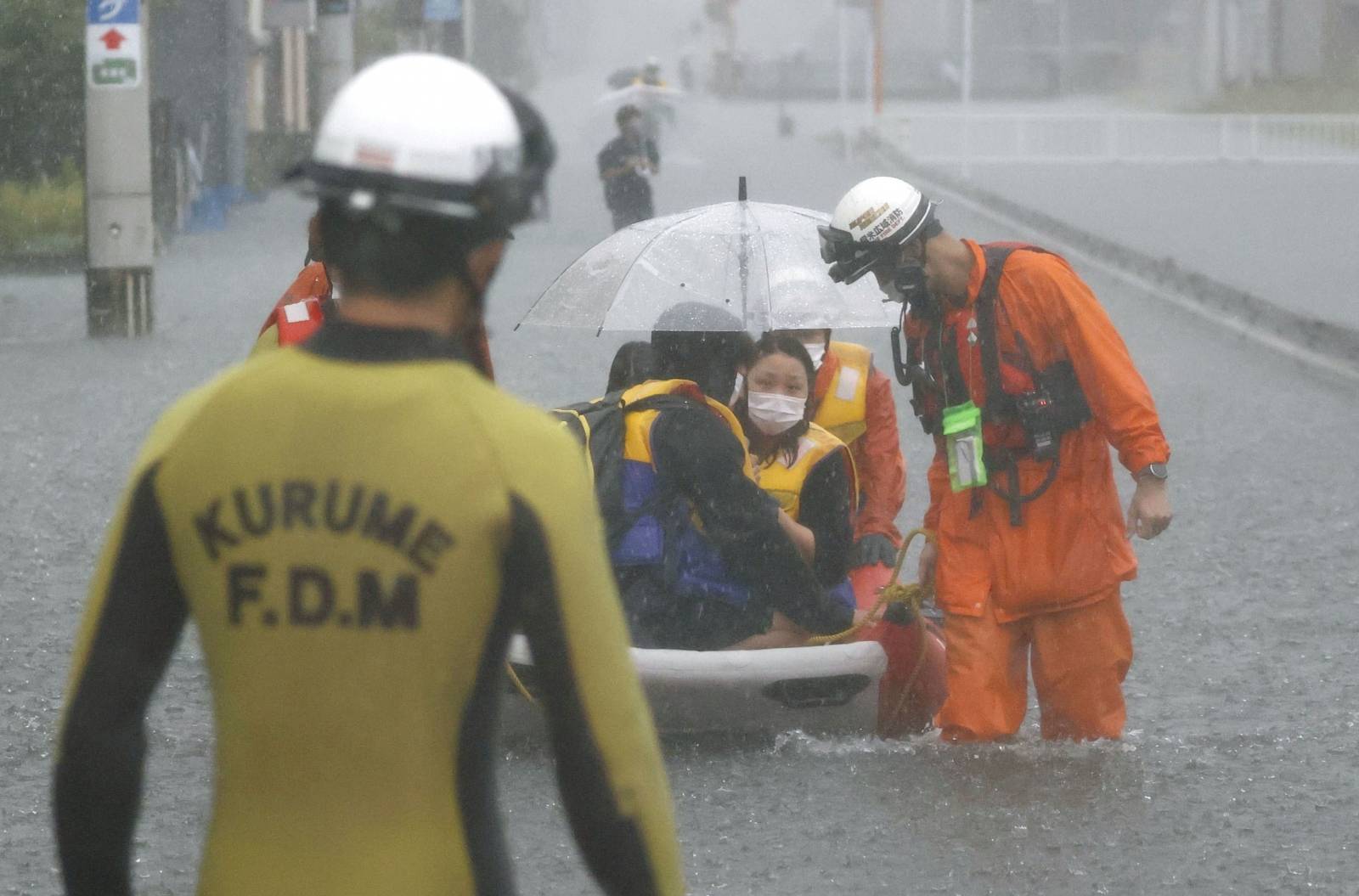 Firefighters transport stranded residents on a boat in a road flooded by heavy rain in Kurume, Japan