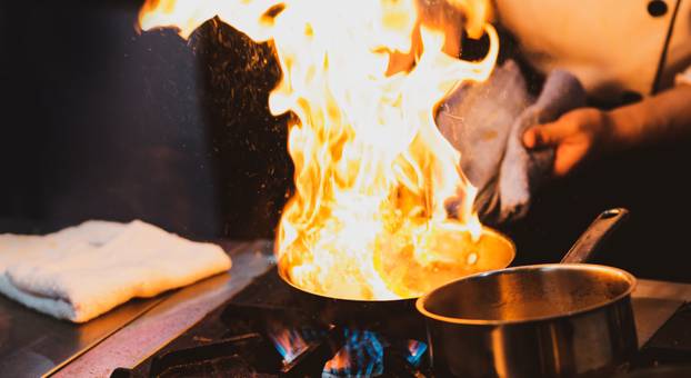 Chef cooking with flame in a frying pan on a kitchen stove
