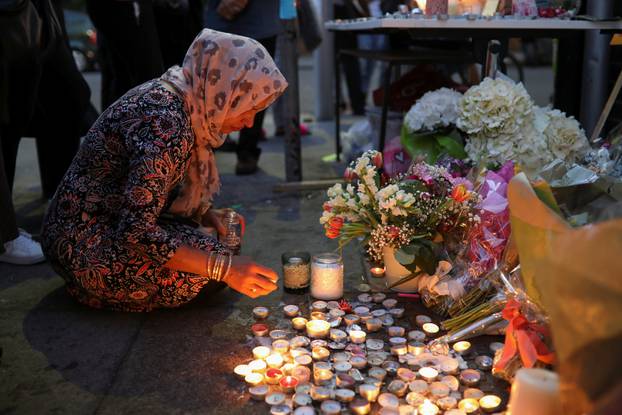 A woman lights a candle next to a wall covered with tributes to and pictures of the victims of the Grenfell apartment tower fire in North Kensington, London