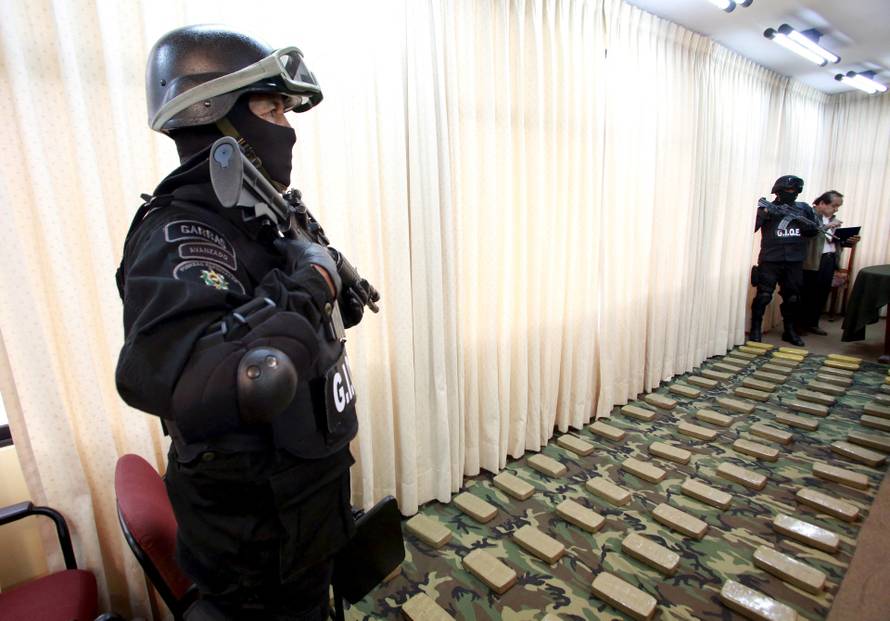 Members of the Bolivian anti-drugs force stand guard next to confiscated packets of cocaine in La Paz