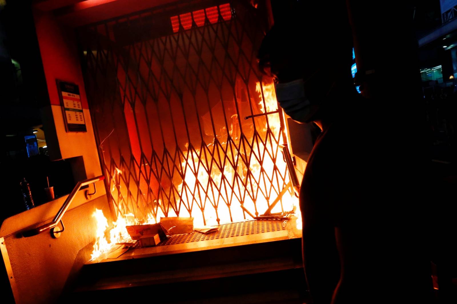 An anti-government protester wears a mask as he sets a fire outside Mong Kok Mass Transit Railway (MTR) station during a demonstration after government's ban on face masks under emergency law, at Mong Kok