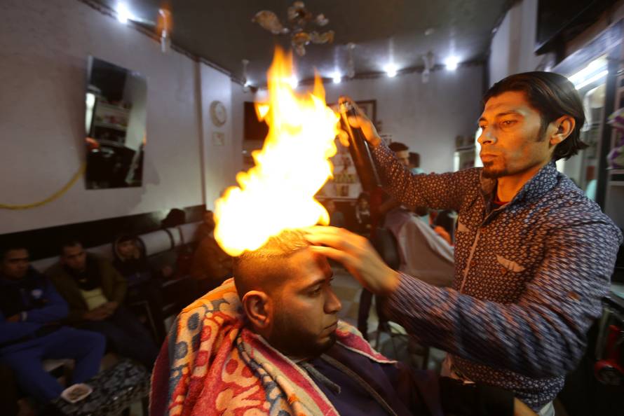 Palestinian barber Ramadan Odwan styles and straightens the hair of a customer with fire at his salon in Rafah, in the southern Gaza Strip