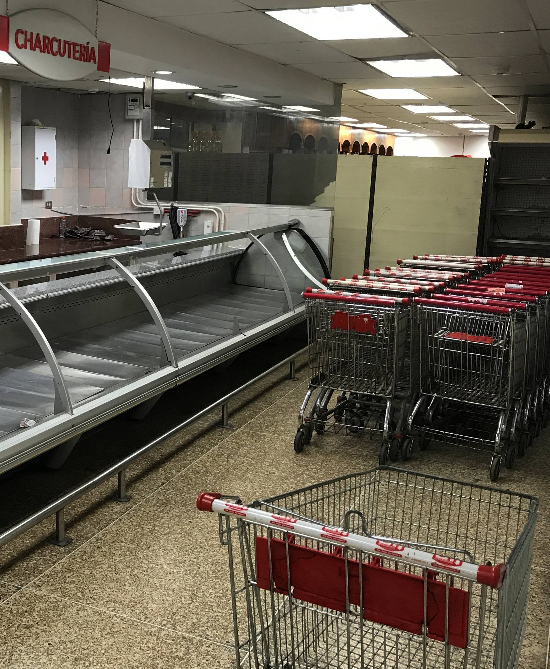 Stacked shopping carts are seen next to empty refrigerators at the deli area at a supermarket in Caracas