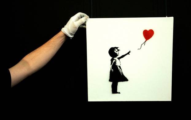 Gallery technician adjusts Banksy's artwork "Balloon Girl" at Sotheby's in London