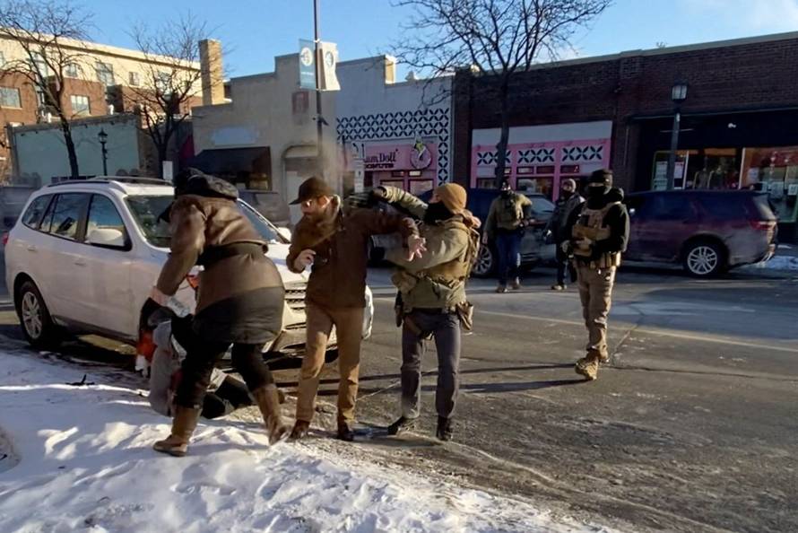 Law enforcement officers kneel next to the body of a man who was shot when federal agents were trying to detain him in Minneapolis