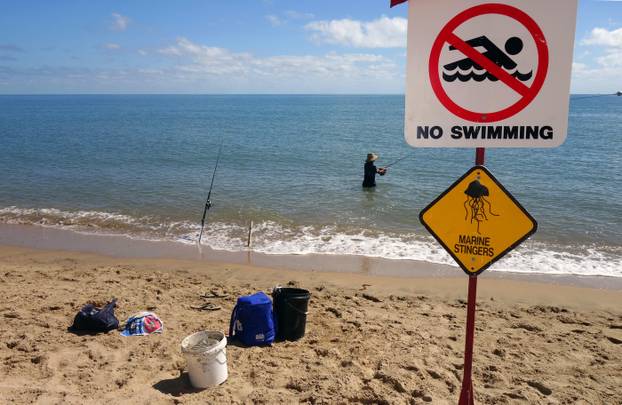Man fishing despite No Swimming - Marine Stingers sign, Holloways Beach, Cairns, Queensland, Australia. No MR or PR