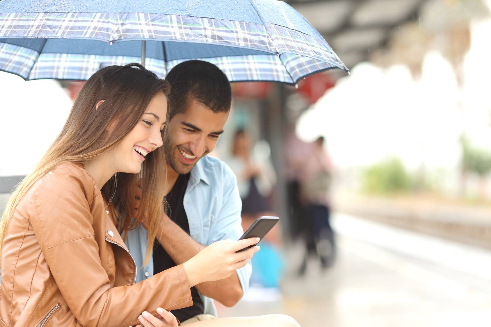 Interracial couple sharing a phone in a train station