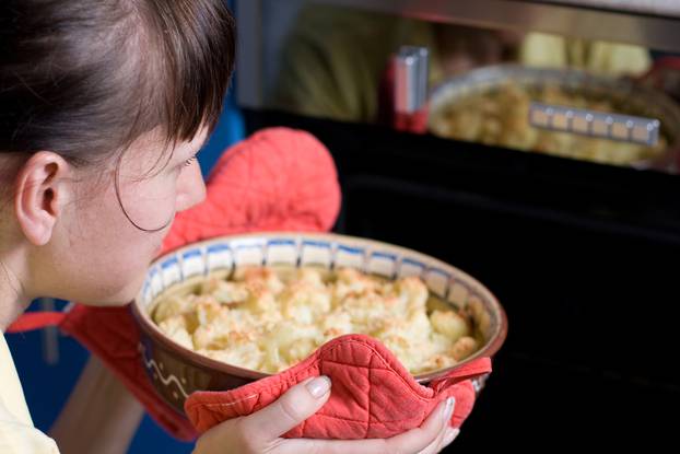 Young woman placing cauliflower into the stove