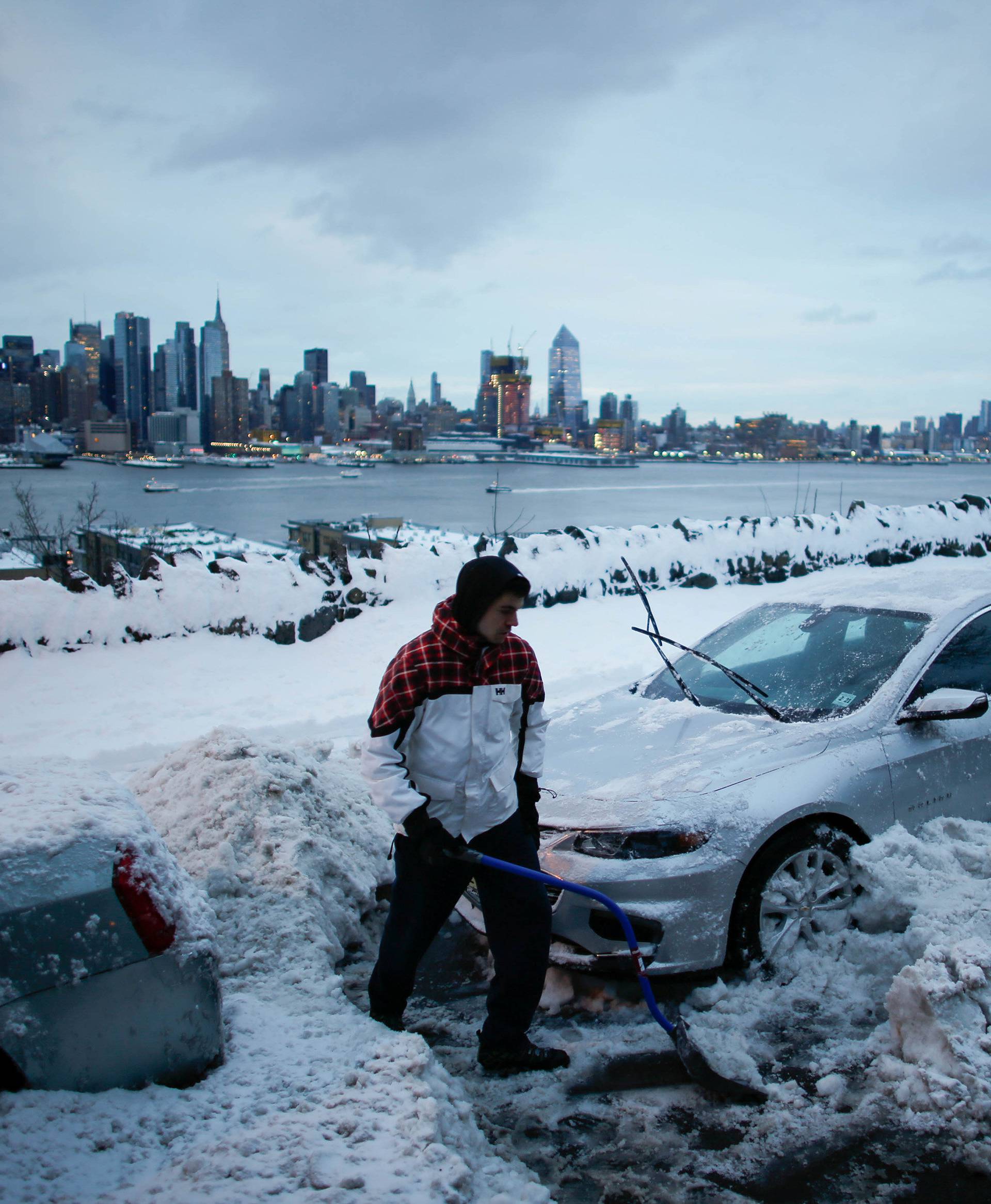 Residents clear their cars and street of snow in Weehawken, New Jersey, as the skyline of Manhattan and the Hudson River are seen after a snowstorm in New York