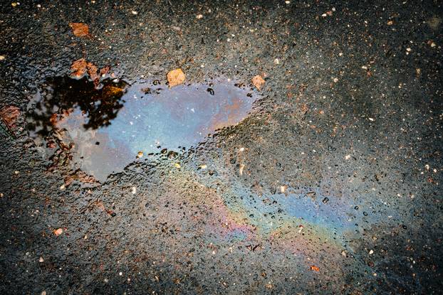 Oil stain on an asphalt road in a puddle in sunlight.