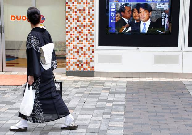 Pedestrian walks past a TV set showing news about North Korea