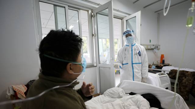 Medical worker in protective suit interacts with a patient inside an isolated ward at Jinyintan Hospital in Wuhan