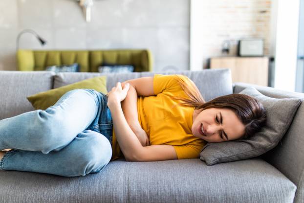 Sick woman lying on sofa in the living room with stomach ache