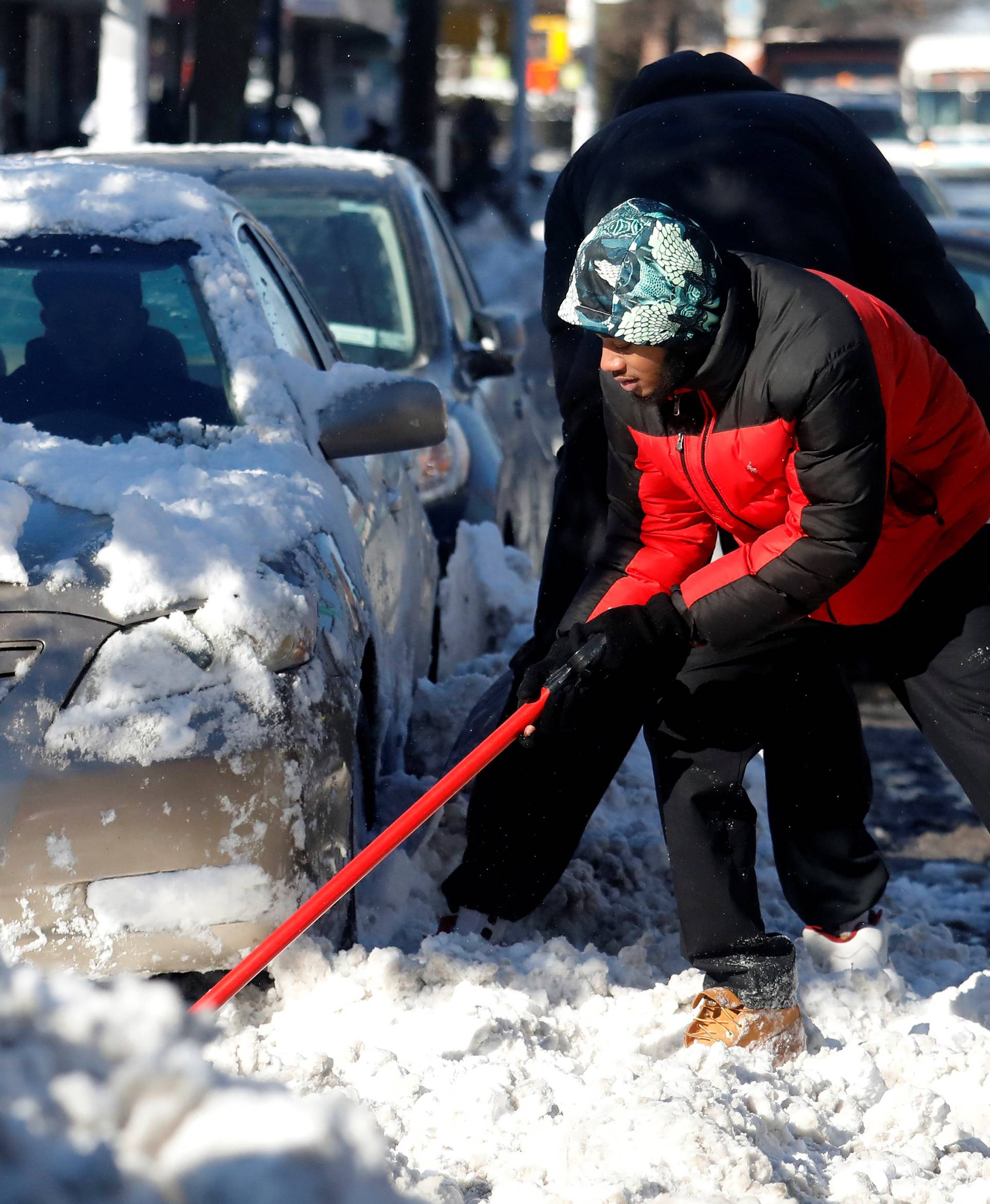 Men shovel snow from a car following winter snow Storm Grayson in the Queens borough of New York