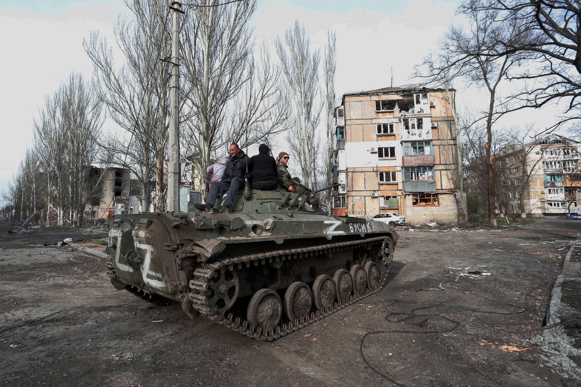 Service members of pro-Russian troops and civilians sit atop of an armoured vehicle in Mariupol