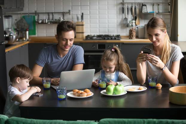 Parents,Using,Laptop,And,Smartphones,Having,Breakfast,With,Children,,Smiling
