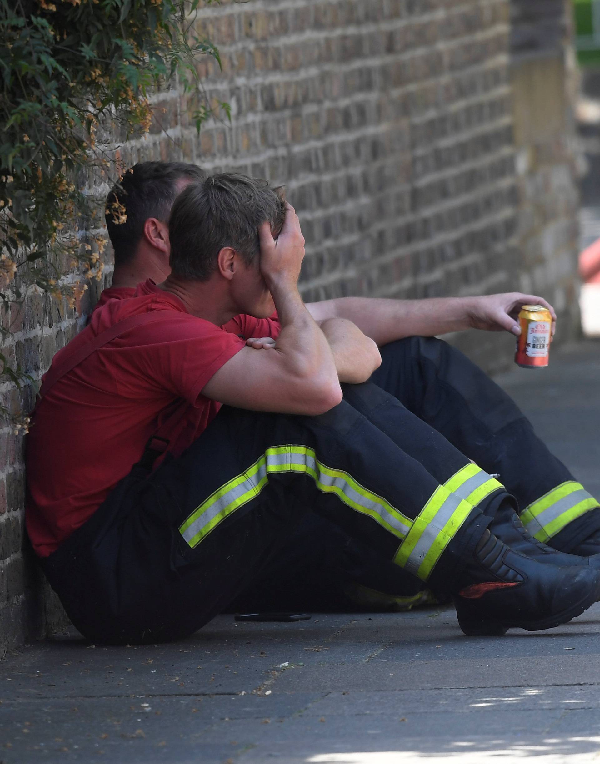 Firefighters rest near a tower block, severely damaged in a serious fire, in north Kensington, West London