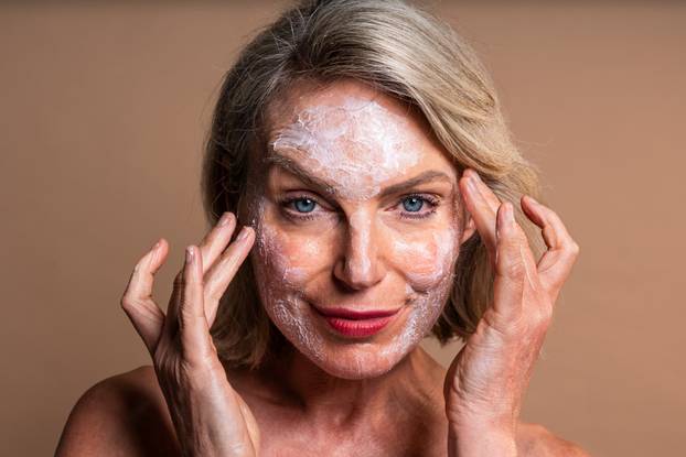 Beauty portrait of beautiful mature woman, concepts about cosmetics, skincare and wellness. Mature woman applying cosmetic cream on face for skincare and wellness
