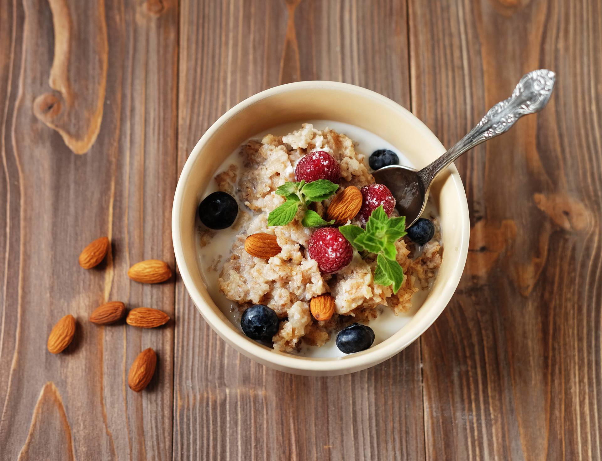 Oatmeal porridge in bowl topped with fresh blueberries and raspberries on wooden table.