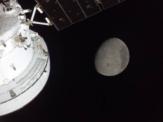 NASA’s Orion spacecraft is seen in the foreground, lit up by the Sun as a first quarter Moon is visible behind it