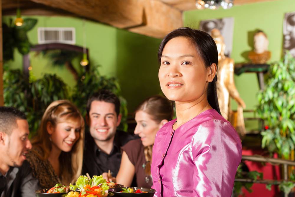 Young,People,Eating,In,A,Thai,Restaurant;,The,Waitress,Brings