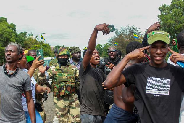 People pose with soldiers as they celebrate in support of the putschists in a street of Libreville