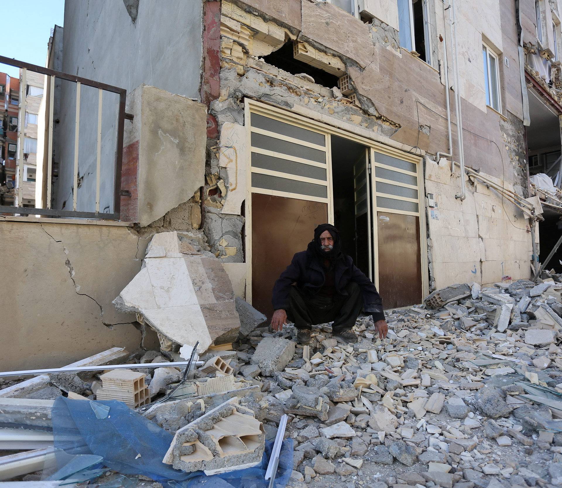 A man sits outside a damaged belonging following an earthquake in Sarpol-e Zahab county in Kermanshah