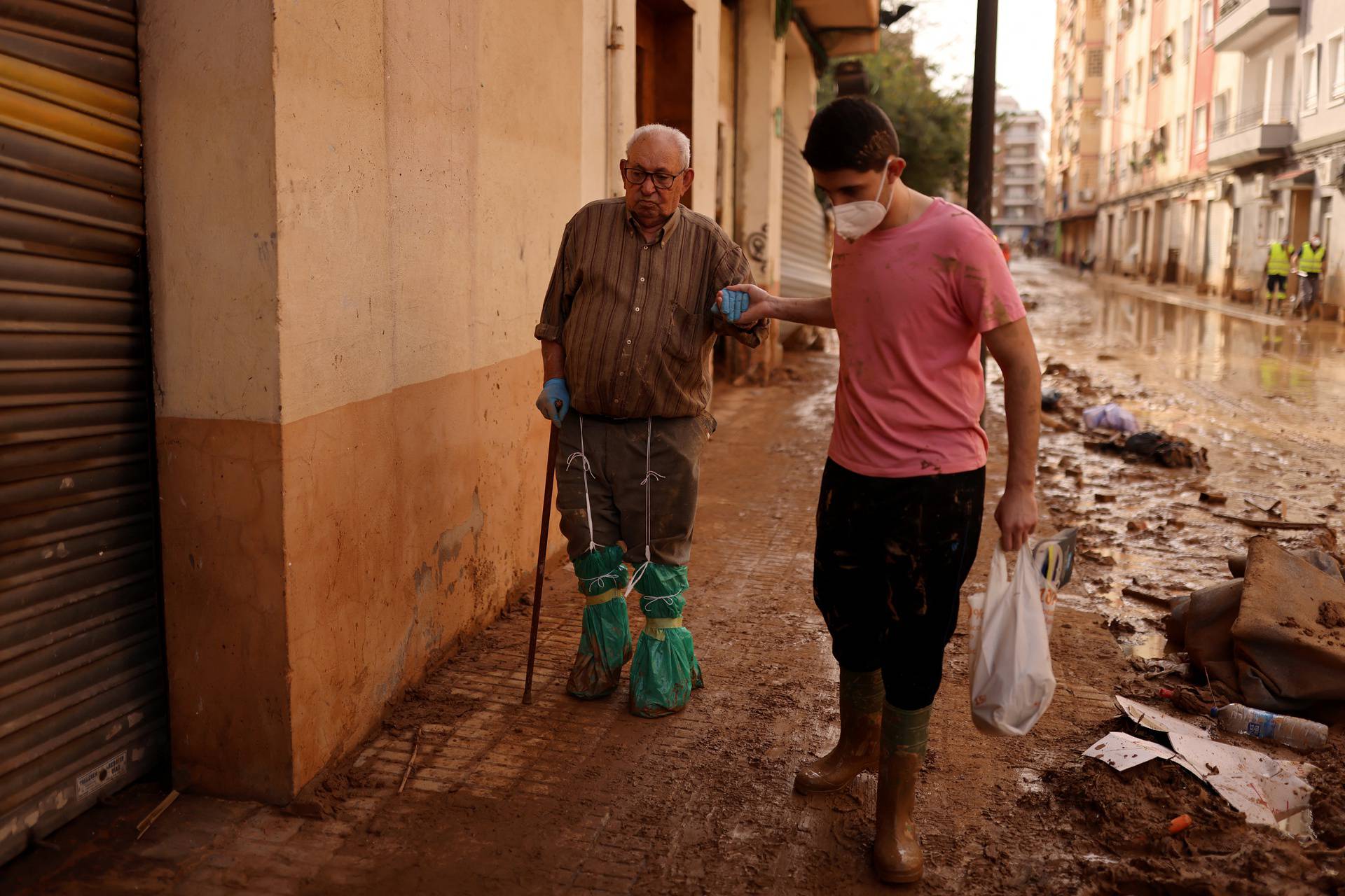 Cristobal Martinez, an 87-year-old resident, is assisted by his grandson as he walks amid mud and debris near his house in Paiporta