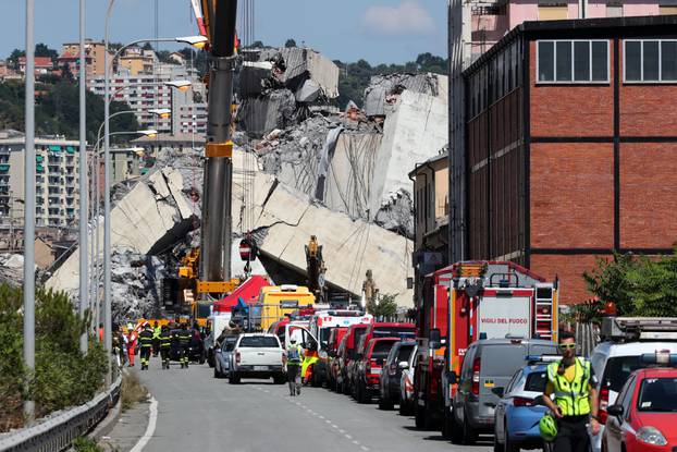 Firefighters and rescue workers stand at the site of a collapsed Morandi Bridge in the port city of Genoa