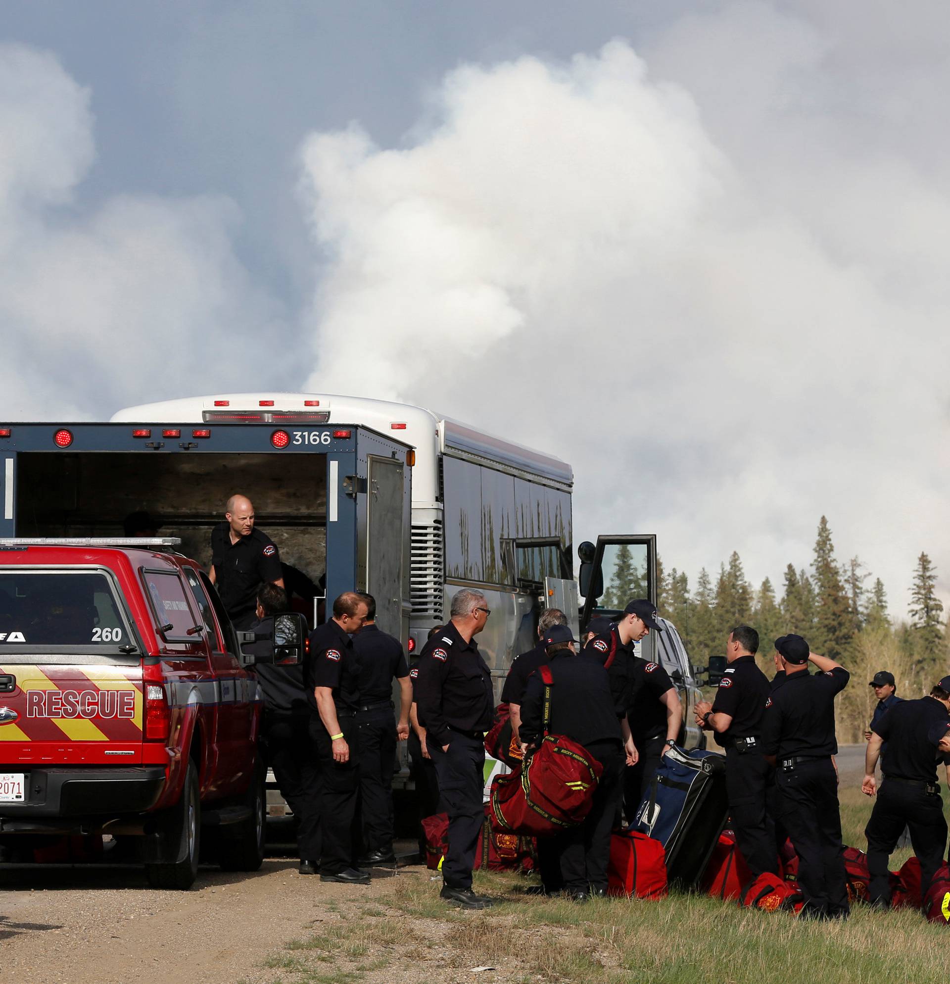 Firefighters unload equipment as smoke rises from nearby wildfires near Fort McMurray