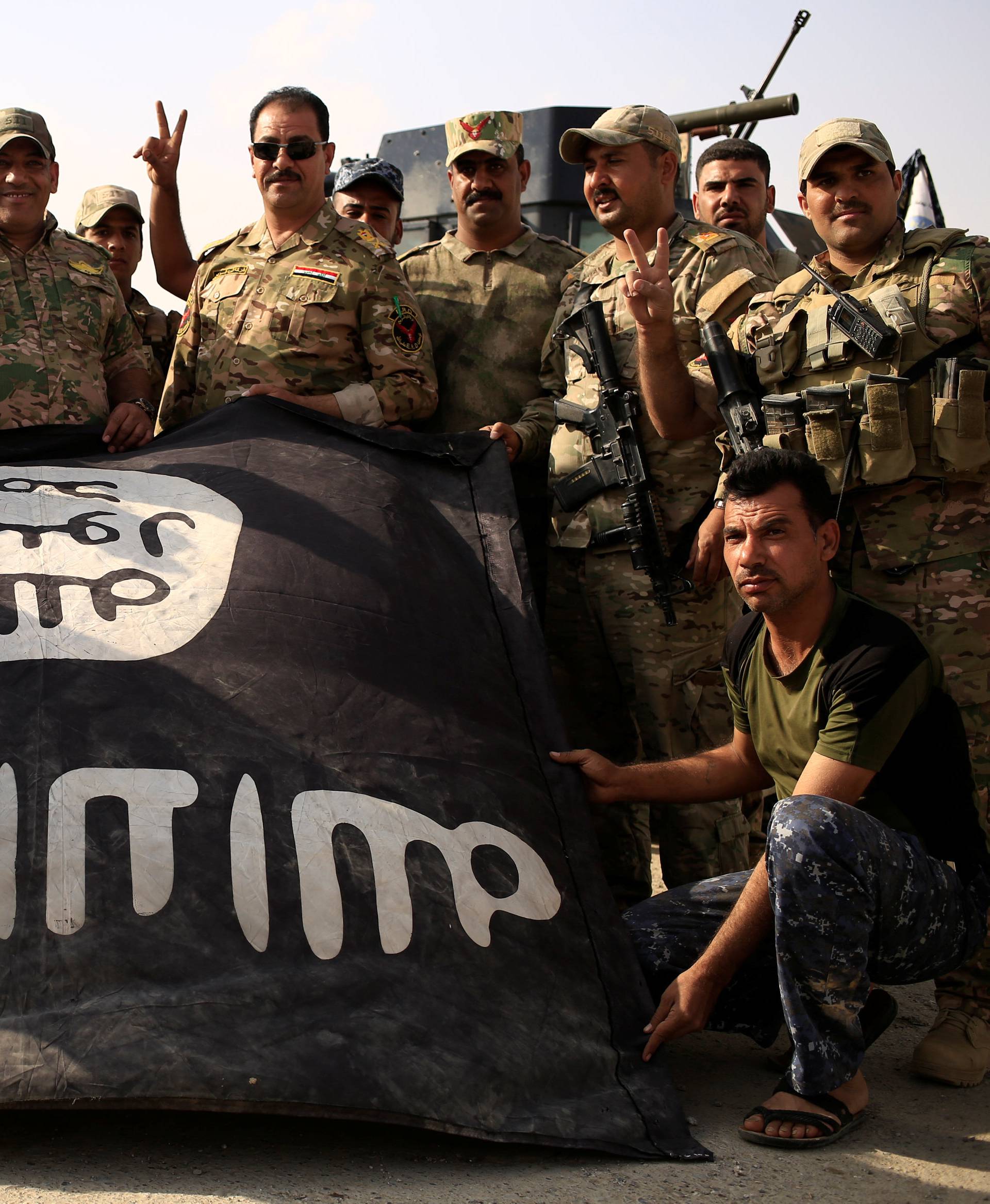 Iraqi soldiers celebrate as they pose with the Islamic State flag along a street of the town of al-Shura