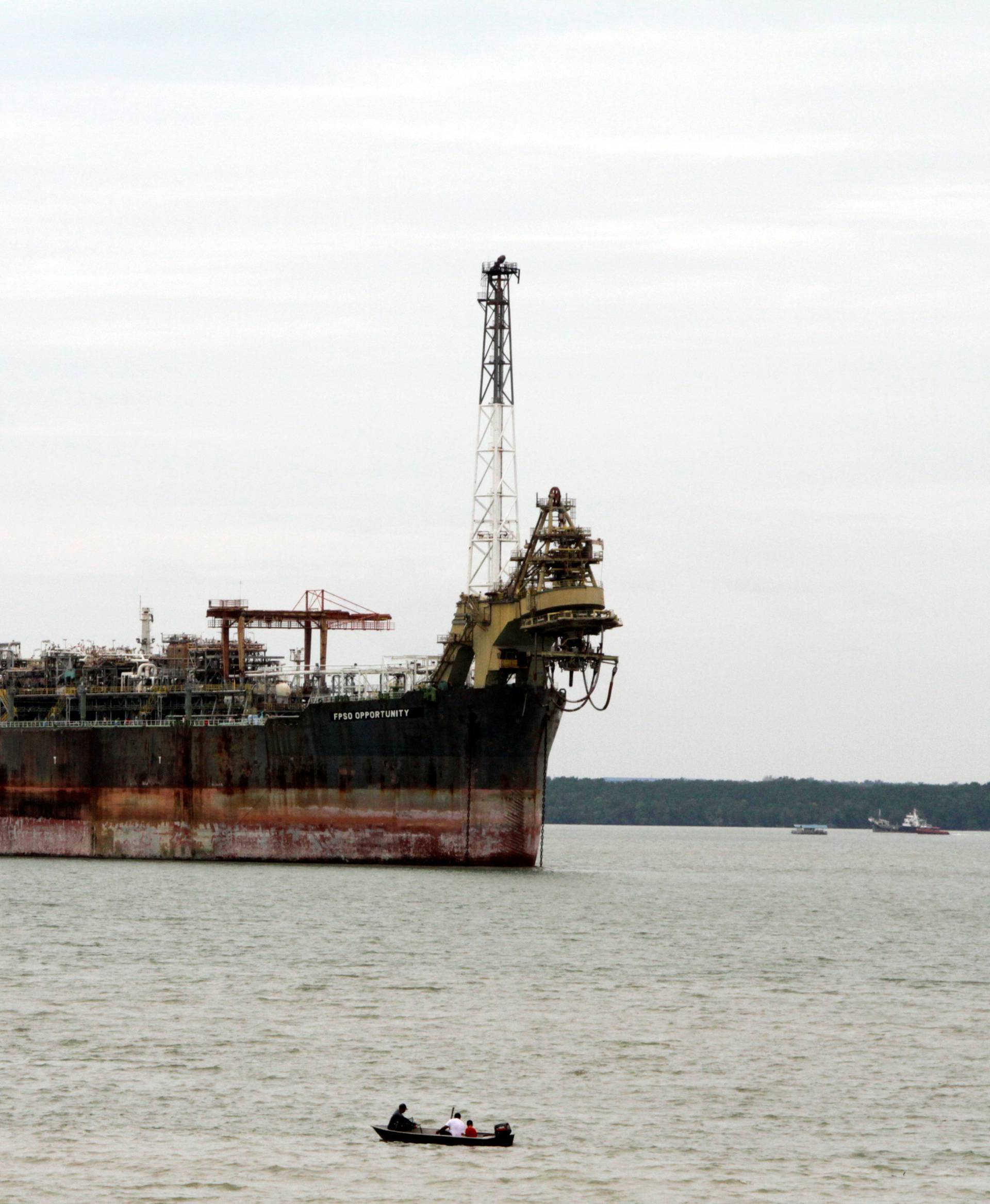 A fishing boat passes in front of the laid-up FPSO Opportunity in the Johor river
