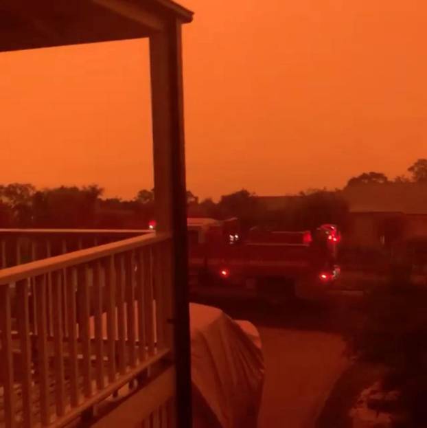 A fire engine drives past homes as the sky is tinted red as surrounding bushfires close in on the town of Mallacoota, Victoria, Australia