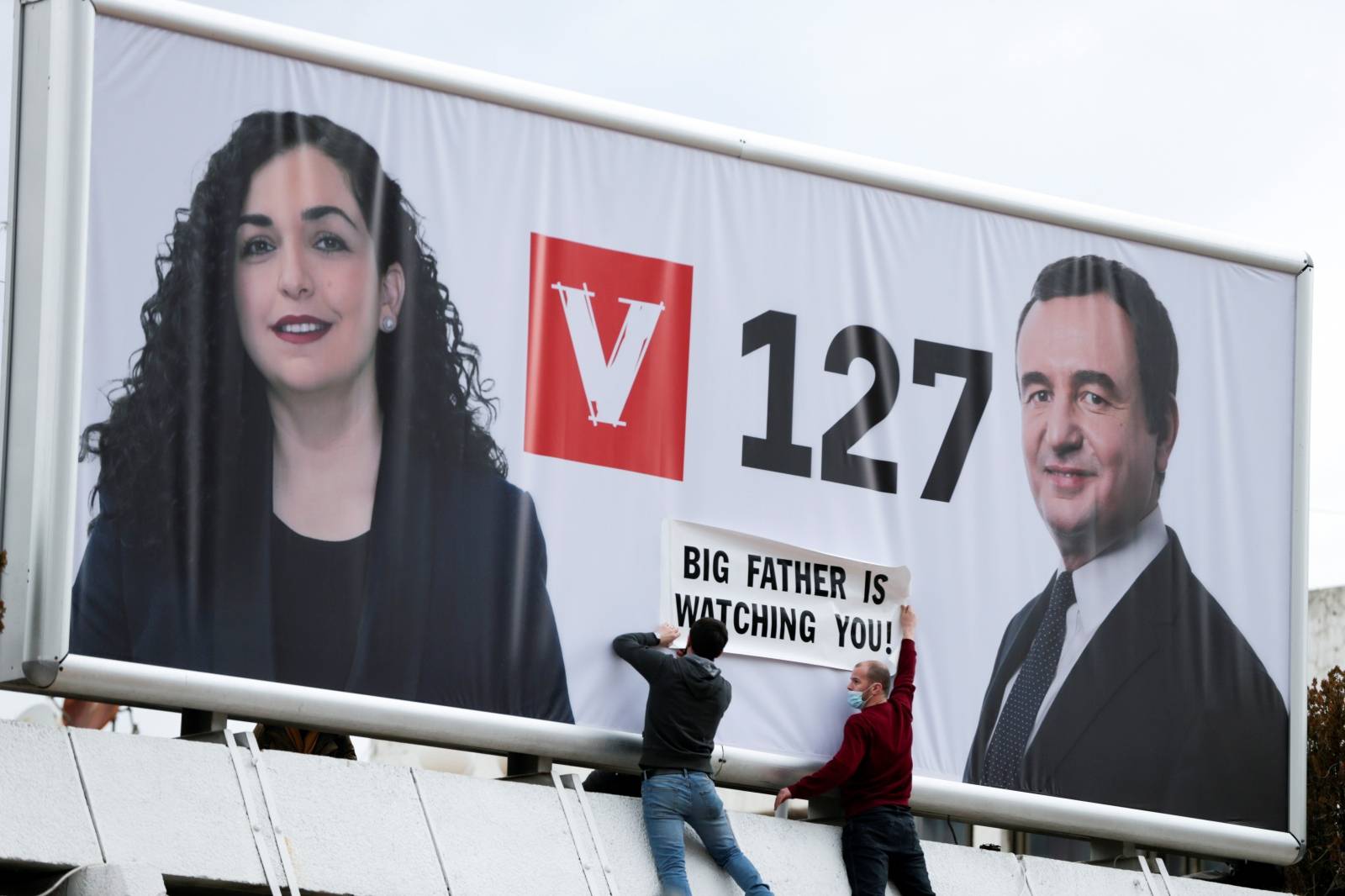 People place a slogan on the poster of Albin Kurti, leader of the Self-Determination movement (Vetevendosje), and the Kosovo's acting president, Vjosa Osmani, in Pristina