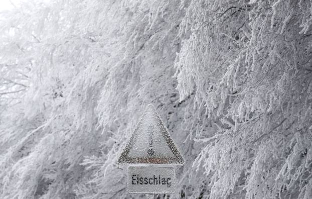 A warning sign reads "beware of icicles" beside snow and ice covered trees near a street towards the Feldberg mountain, outside Frankfurt