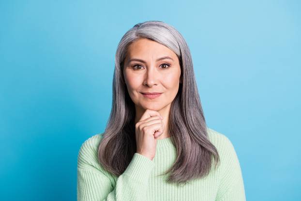 Portrait of confident aged lady dressed green sweater touch chin isolated on blue color background