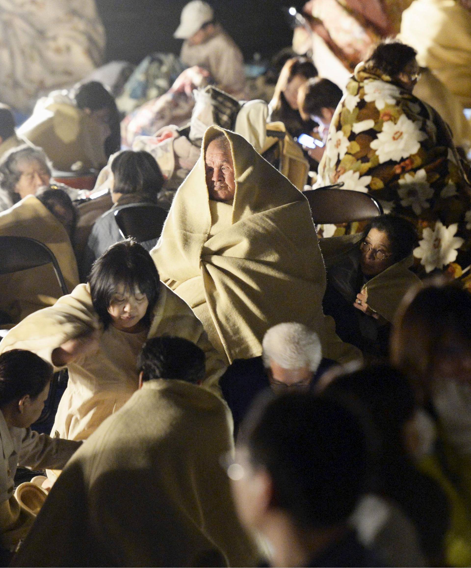 Local residents wrap themselves in blankets as they sit on the road in front of the town office building after an earthquake in Mashiki town, Kumamoto prefecture, Japan