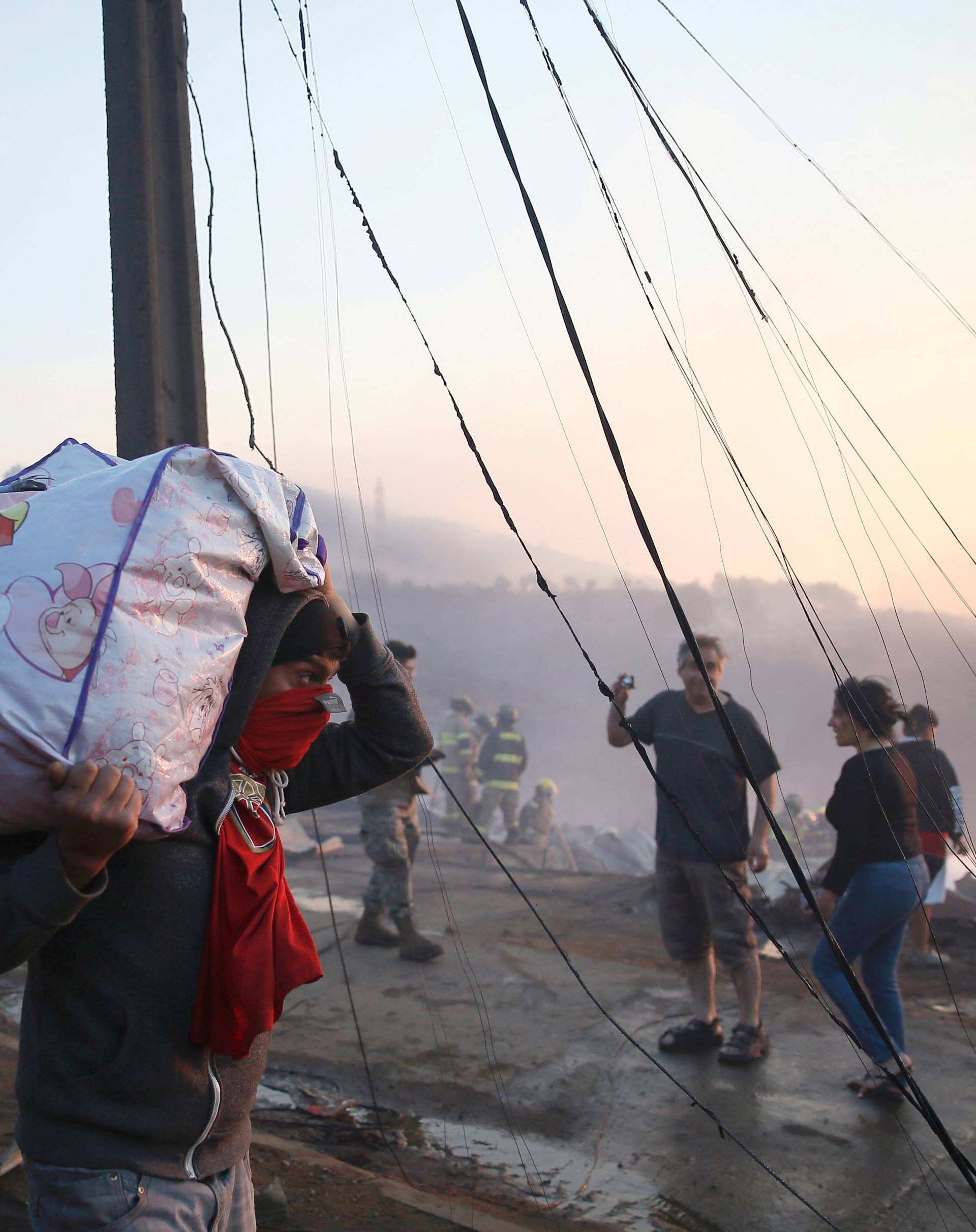 A resident is seen walking while carrying his belongings in front of the remains of burned houses on a hill, where more than 100 homes were burned due to a forest fire but there have been no reports of death, local authorities said in Valparaiso, Chile