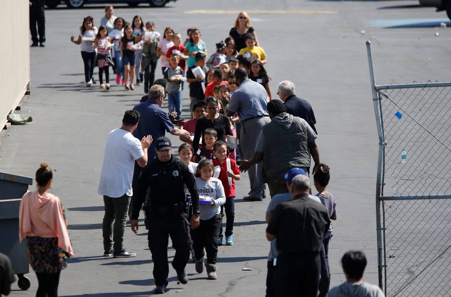 Students who were evacuated after a shooting at North Park Elementary School walk past well-wishers to be reunited with their waiting parents at a high school in San Bernardino