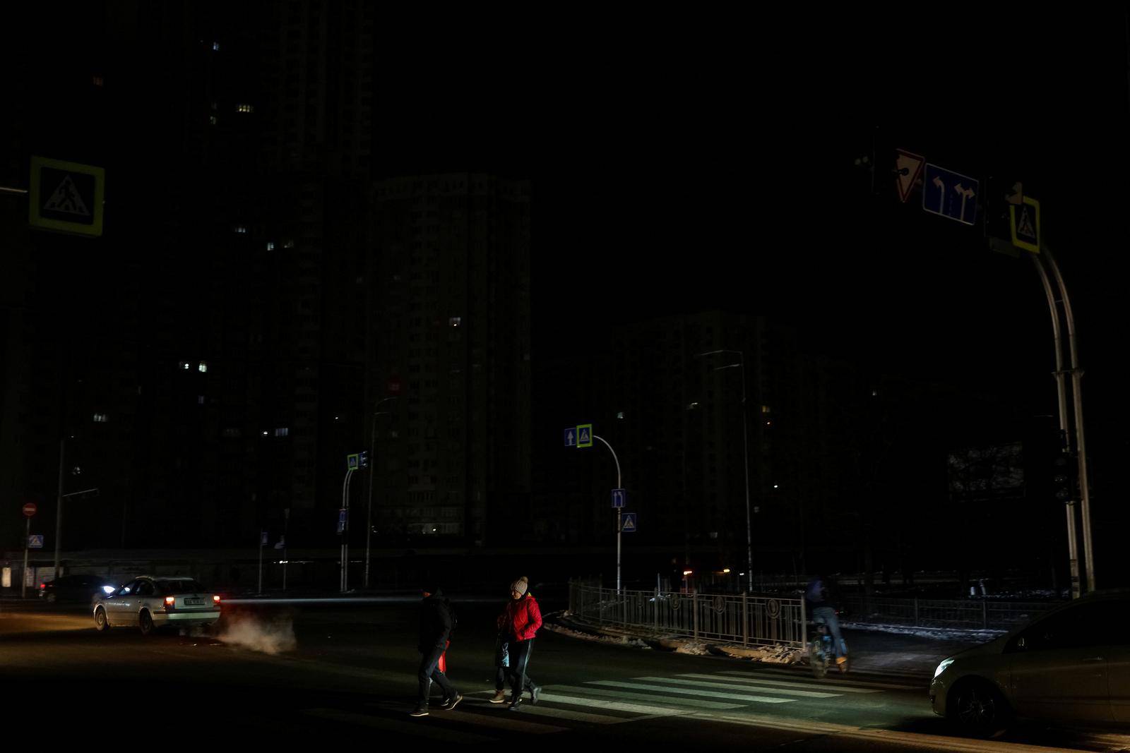 People cross a street without electricity after critical civil infrastructure was hit by Russian missile attacks in Kyiv