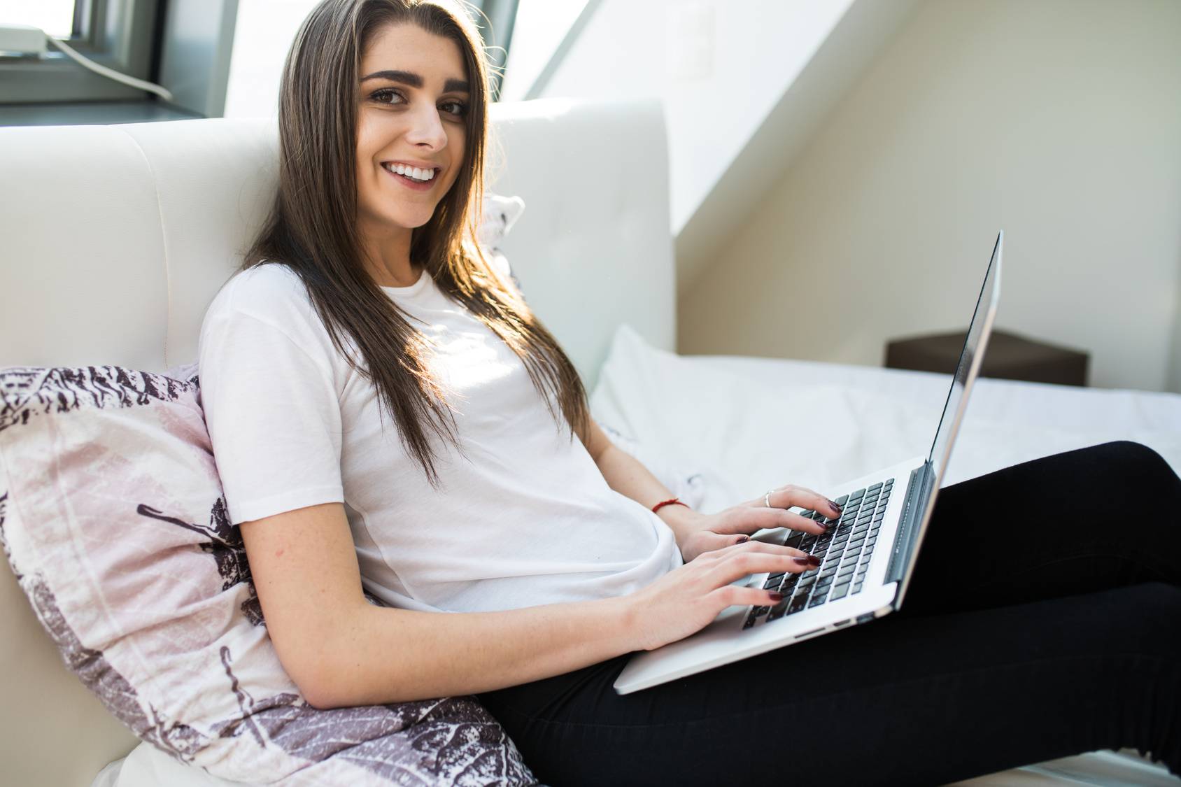 Happy young woman with laptop lying on bed