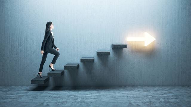 Young,Businesswoman,Moving,Up,On,Stairs,With,Arrow,On,Gray